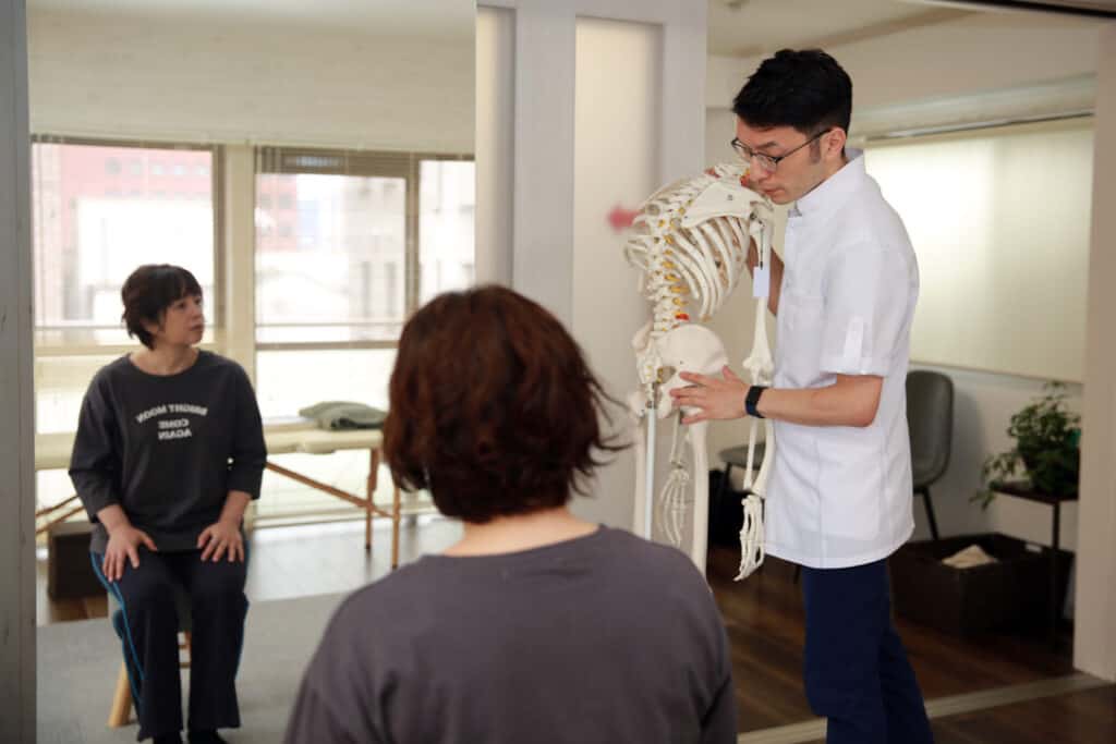 骨格模型を用いて施術の説明をする施術者